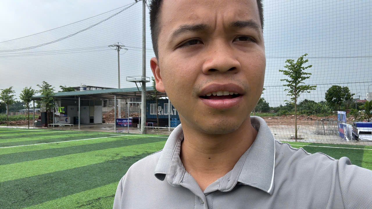 Nguyễn Đức Toàn tại một sân cỏ nhân tạo với hệ thống lưới chắn và nhà điều hành phía sau